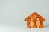 Dřevěný dům s figurami muže a ženy uvnitř na šedém pozadí s prázdným prostorem pro text.