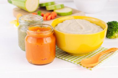 Doğal bebek maması konsepti. Kasede farklı sebze püresi çeşitleri ve malzemelerin yanında beyaz ahşap arka planda kavanozlar. Seçici odak.