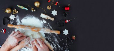 Aile tatili aktivitesi. Baba ve çocuğun ellerinin siyah arka planda Noel kurabiyesi yaparken görüntüsü ve mesaj için boş bir alan. Düz yatıyordu.