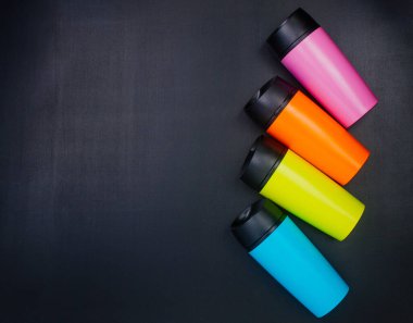 Tebeşir tahtası arka planında çok renkli termo bardaklar ve metin için boş alan. Üst manzara, düz uzanma.