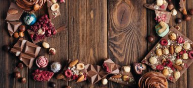 Kırık sütlü çikolataların çerçevesi fındık ve sublimleşmiş dutlar ve kırsal ahşap arka planda çikolata şekerlemeleri, yazı için boş alan; üst görünüm, düz yatıyordu