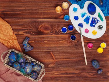 Mutlu Paskalya Kartı: Galaksi Paskalya yumurtaları ve paleti ile rustik ahşap zemin üzerinde boyalar ile metin için boş alan; üst görünüm, düz yatar