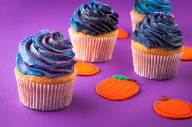 Cadılar Bayramı kekleri koyu kremalı menekşe arkaplanlı ve balkabaklı. Seçici odak.