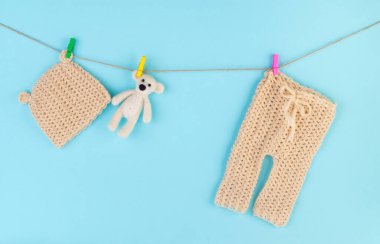 Yeni doğmuş bebek şapkası ve pantolonu açık mavi arka planda ayı oyuncağıyla mandalların üzerinde. 