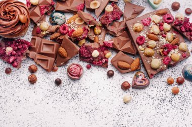 Kırık sütlü çikolatalar, fındıklı ve süblimleşmiş meyveler ve çikolatalı şekerler, dokulu gri arka planda, metin için boş alan, üst görünüm, düz yatış
