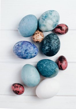 Mermer taş efektli Paskalya yumurtaları beyaz ahşap arka planda doğal boya kartuşu çiçeğiyle boyanmış. Üst manzara, düz uzanma.