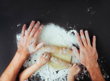 Baba ve çocuğun elleri siyah zemin üzerinde büyük ve küçük oklavalarla hamuru yuvarlarken ve mesaj için boşluk bırakırken en iyi görüntü. Düz yatıyordu.