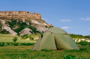 Kireçtaşı dağ kayalıklarının önündeki çayırda turist çadırı; seçici odak
