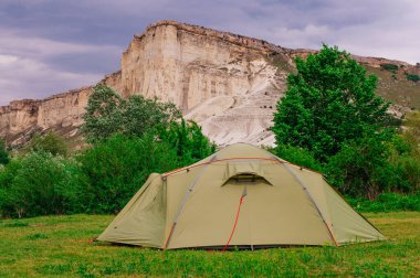 Kireçtaşı dağ kayalıklarının önündeki çayırda turist çadırı; seçici odak