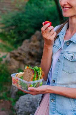 Sağlıklı gıda kavramı: Genç hippi kız beslenme çantasından sandviç, cips, meyve ve sebze yiyor.