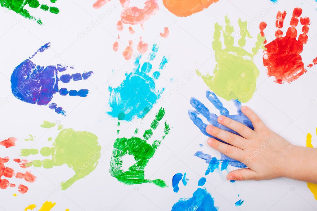 Kid's hand making colored handprints on white background. Top view, flat lay.