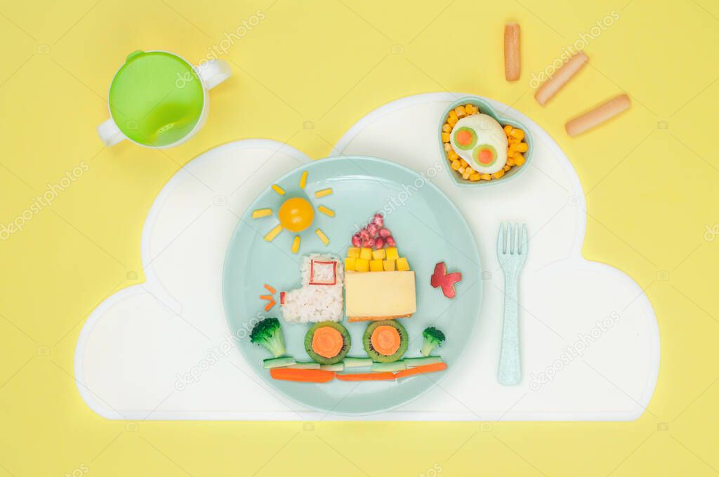 Kids food art concept: car from rice, sandwich and fresh fruits and vegetables on the plate with cloud napkin on the yellow background; top view, flat lay