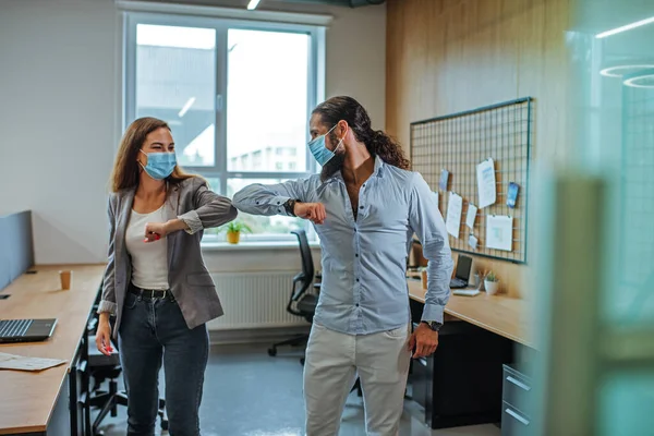 Informal greeting elbow bump by business people in the medical masks in the office during outbreak of the global pandemic COVID-19. Avoiding handshakes in a new normal. Selective focus on the man.