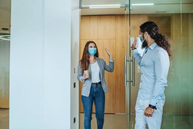 Küresel COVID-19 salgını sırasında sağlık maskeli genç iş adamları ofiste birbirlerini selamlıyorlar. Yeni normal bir şekilde el sıkışmaktan kaçınıyorum..