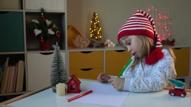 모자를 쓴 어린 소녀가 산타클로스에게 편지를 쓰는 모습 — 비디오