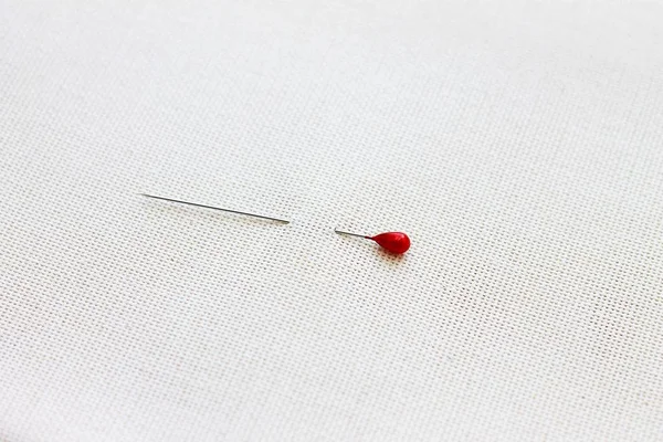 sharp pin with a red head pinned to a light fabric concept of needlework, sewing and creativity