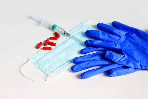 On a white background disposable gloves, a protective mask, tablets, and a syringe