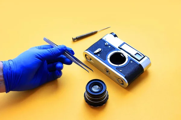 Vintage camera lens and tools, tweezers and a screwdriver with yellow paper background, camera repair concept.