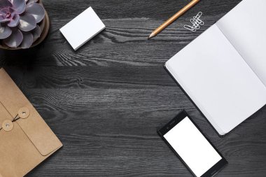 Ofis, banka donatımı ve metin için yer siyah bir masa. Masanın üstünde bir kalem, ataç, bir dizüstü bilgisayar, bir zarf ve bir tencerede bir bitki olduğunu