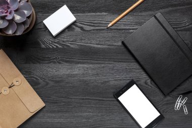 Ofis, banka donatımı ve metin için yer siyah bir masa. Masanın üstünde bir kalem, ataç, bir dizüstü bilgisayar, bir zarf ve bir tencerede bir bitki olduğunu