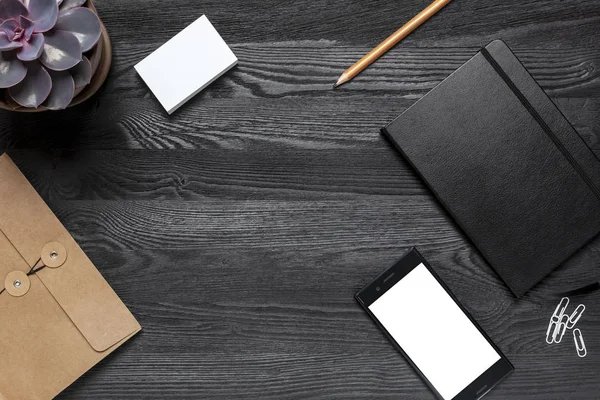 Ofis, banka donatımı ve metin için yer siyah bir masa. Masanın üstünde bir kalem, ataç, bir dizüstü bilgisayar, bir zarf ve bir tencerede bir bitki olduğunu