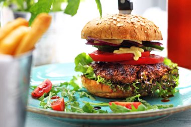 Bir tabak üzerinde servis edilen bir ızgara sığır balığı, domates, salatalık, marul ve sos ile Burger.