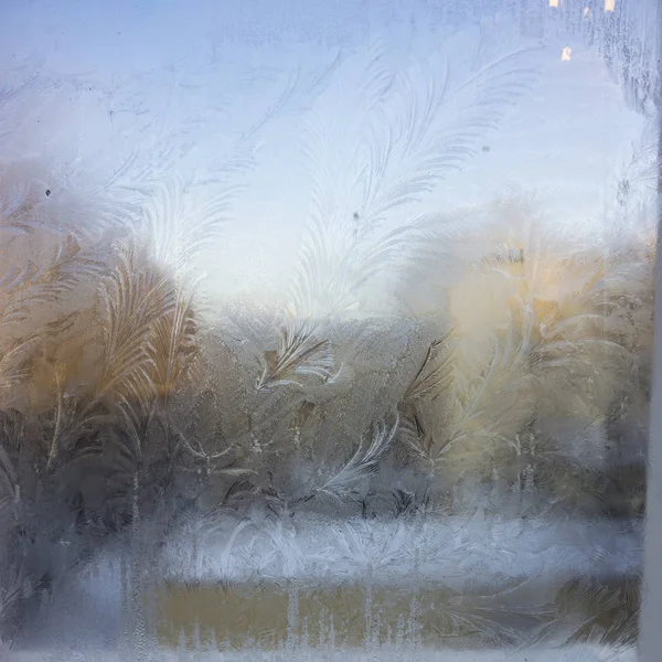 Vista da antiga casa da cidade a partir de uma janela de inverno congelada. Padrões de gelo de textura em vidro. Foco seletivo . — Fotografia de Stock