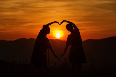 Dişi eller, kalp şeklinde gökyüzüne karşı güneş ışınlarını uzatıyorlar. Akşamları dağlarda kalp şeklinde eller ve tepede güzel güneş ışığı..