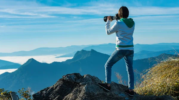 the tourist standing on cliff in front of a sunset and  taking pictures of fog in mountain view around.View of mountains, winter landscape with foggy hills at sunrise