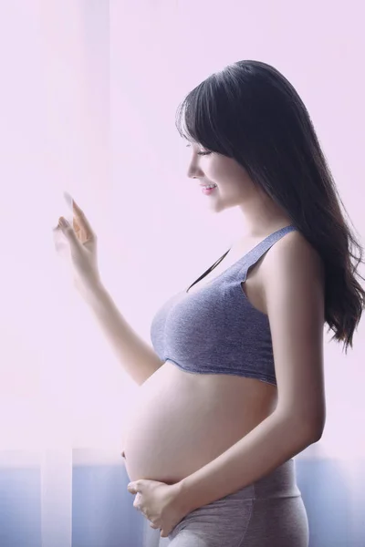 Young Pregnant Asian Woman Holds Her Hands on Her Swollen Belly, Love Concept. Pregnancy, Love, People and Expectation Concept - Happy Pregnant Woman Making Heart Gesture.