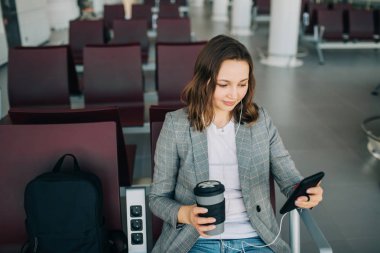 Bekleme alanında oturan kız, akıllı telefon kaydırma.