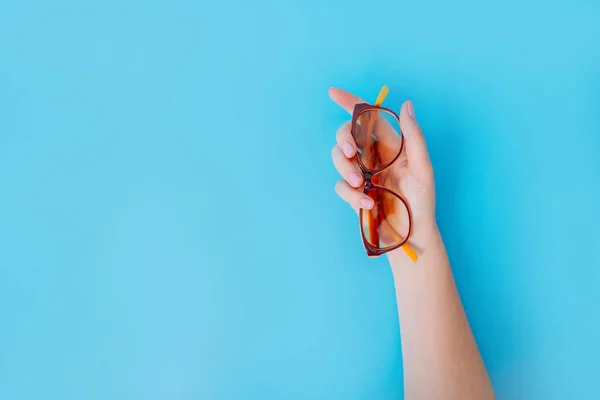 Weibliche Hand hält Brille auf blauem Hintergrund. — Stockfoto