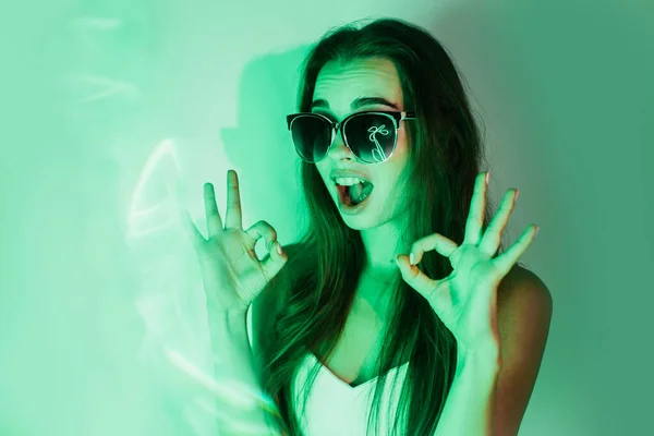 Nachtportret van een meisje in groen neon licht tonen ok. — Stockfoto