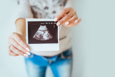 Evde ultrason görüntüsü taşıyan hamile bir kadının yakın çekimi. Hamile karnı.