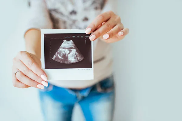 Close-up of pregnant woman at home, holding ultrasound image. Pregnant belly. Stock Picture