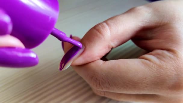Женщина красит ногти фиолетовым лаком — стоковое видео
