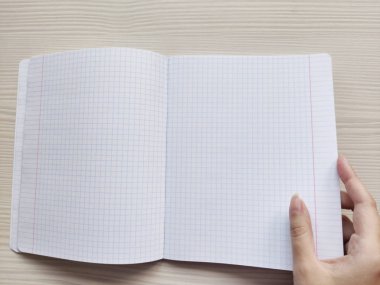 Beyaz açık okul damalı egzersiz kitabı bir kafes içinde ahşap bir masa üzerindedir. Beyaz kadın notsuz bir not defteri açar. Kare ile boş bir not defteri tutan beyaz bir Avrupalı kadının sağ eli