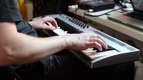 Ein weißer Mann im schwarzen T-Shirt spielt seine Lieblingsmusik auf einem Synthesizer — Stockvideo