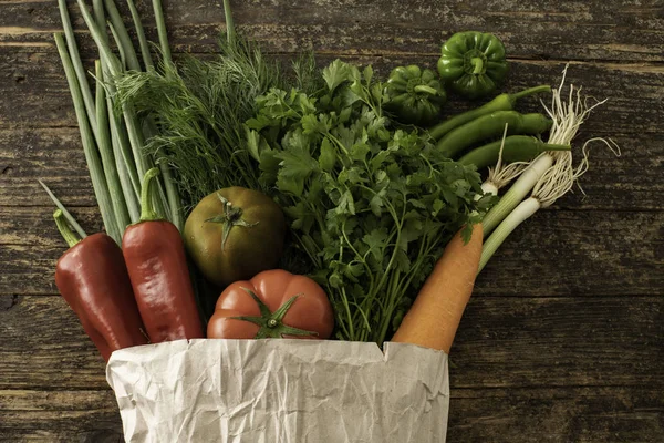 Many farm vegetables on a rustic wooden table and in the paper shooping bag.