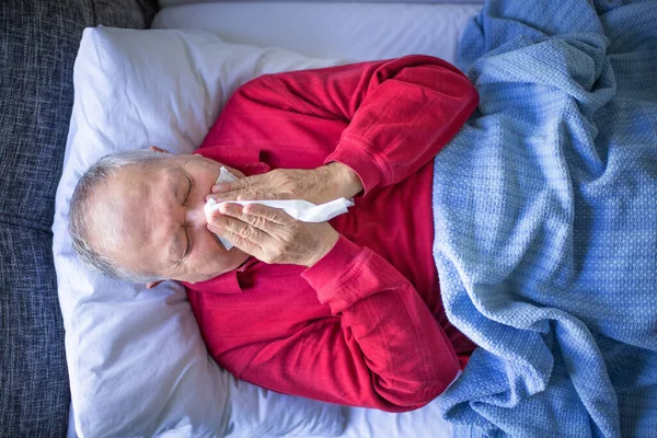 A senior sick man is lying on the bed with fever , illness concept at the bedroom with bed and blanket. Covid 19 at nurse home.