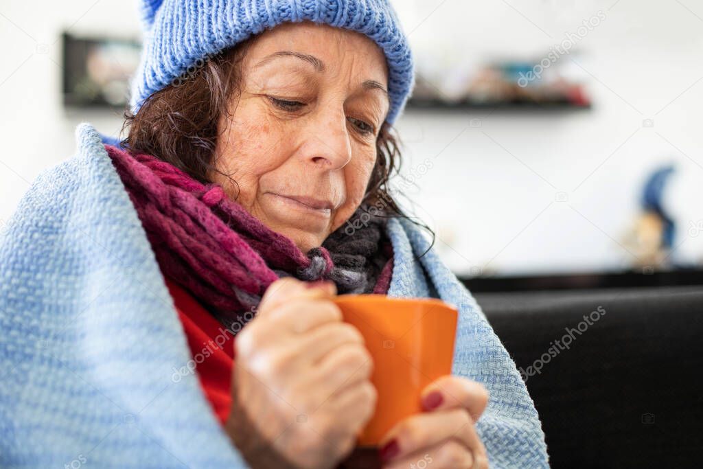 Elderly woman checking her temperature when she is corona, covid 19 and corona virus concept at nursing home with blanket and beret 