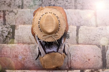 Taştan merdivenlerde oturan bir kadının arkası hasır şapkalı, üst görüşlü bir tatil konsepti.. 