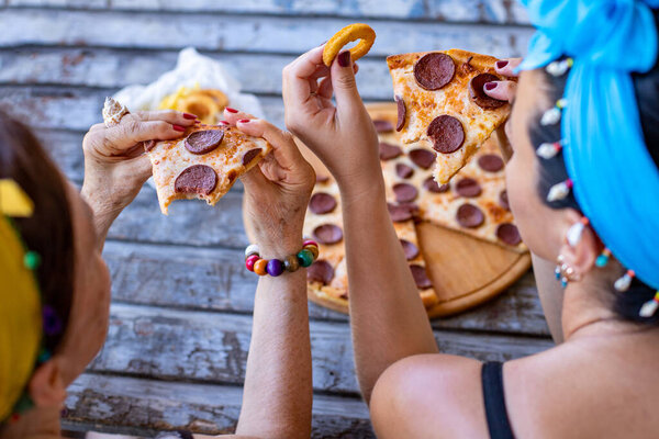 Many hands and side view of two women who are eating pizza on the table. Fast food concept with pepperoni pizza.