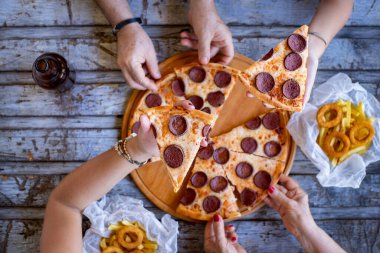 Masada bir sürü el var ve bu arkadaşlar masada pizza yiyorlar. Pepperonili pizza ile fast food konsepti.