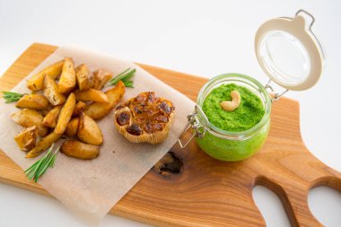 Biberiyeli fırında patates, sarımsak ve ahşap bir tahtada pesto.