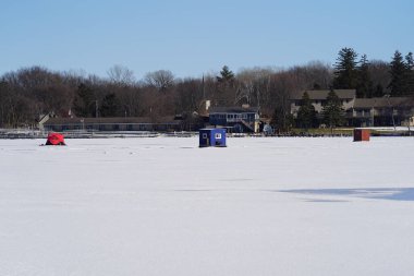Green Lake, Wisconsin USA - January 20, 2024: People ice fishing out on a frozen lake in ice shanties. clipart