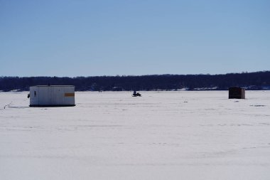 Green Lake, Wisconsin USA - February 11th, 2023: People ice fishing out on a frozen lake in ice shanties. clipart