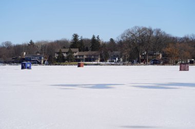 Green Lake, Wisconsin USA - February 11th, 2023: People ice fishing out on a frozen lake in ice shanties. clipart