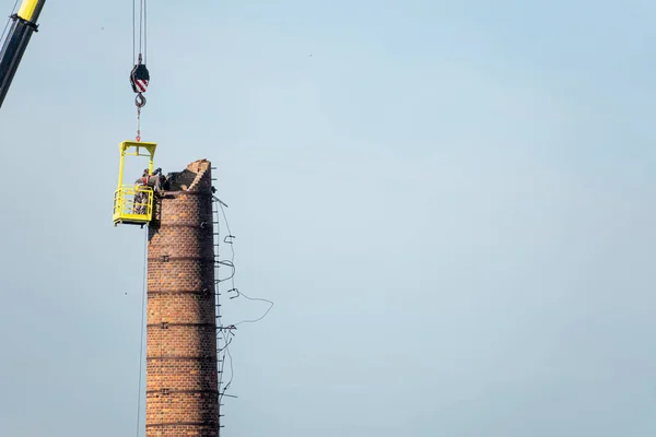 2 men in a basket hanging from a gigantic crane, painstakingly r