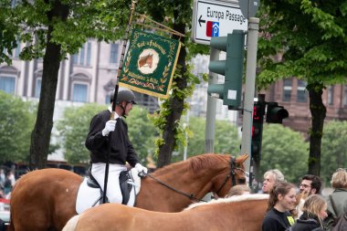 elinde bayrak tutan üniformalı bir atlı geçit törenine öncülük ediyor.